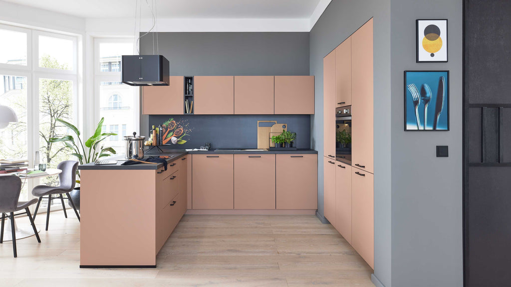 Moderne Küche mit hellen, pinkfarbenen Schränken, schwarz-grauem Arbeitsbereich, Pflanzen und einem Esstisch mit Stühlen.