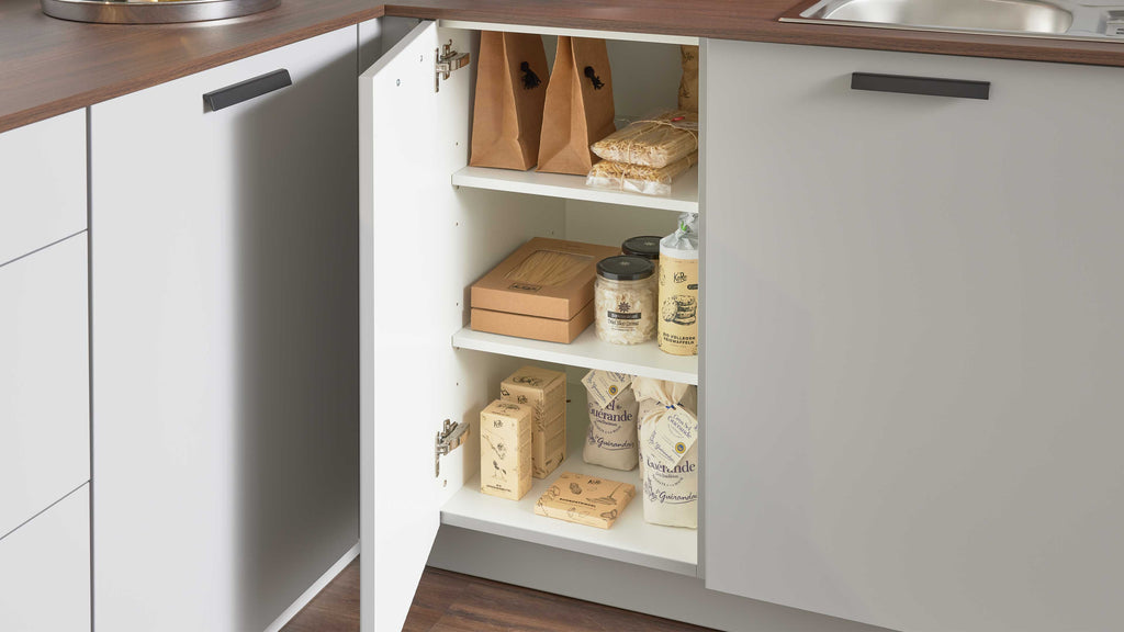 Der geschlossene Küchenschrank mit weißen Türen enthält verschiedene Lebensmittelverpackungen und ein Glas mit Zutaten.