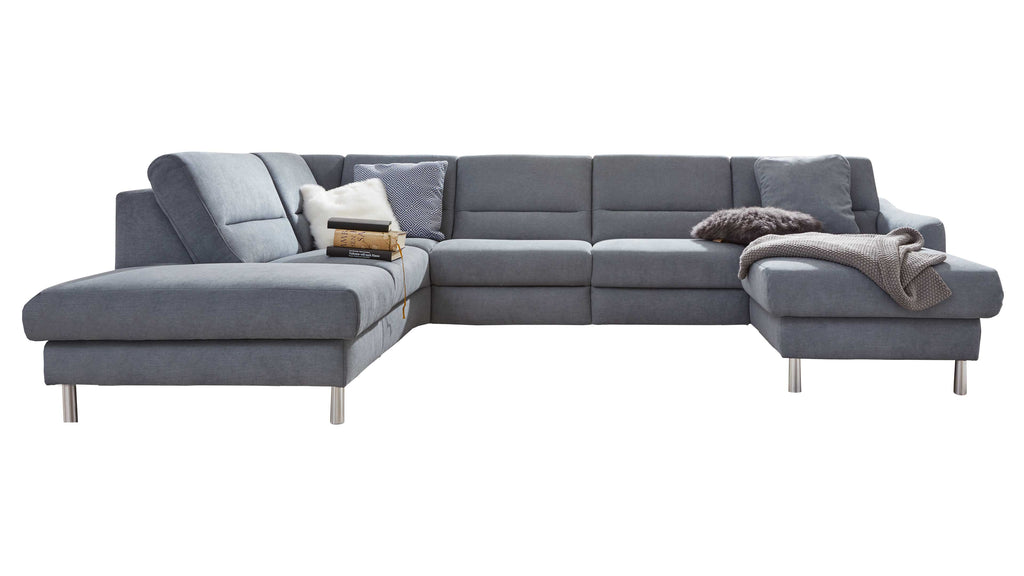 Große grau bezogene Eckcouch mit Metallfüßen, links längere Chaiselongue, rechts kürzerer Ottomane, Kissen, Decke und Bücher.