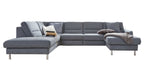 Große grau bezogene Eckcouch mit Metallfüßen, links längere Chaiselongue, rechts kürzerer Ottomane, Kissen, Decke und Bücher.