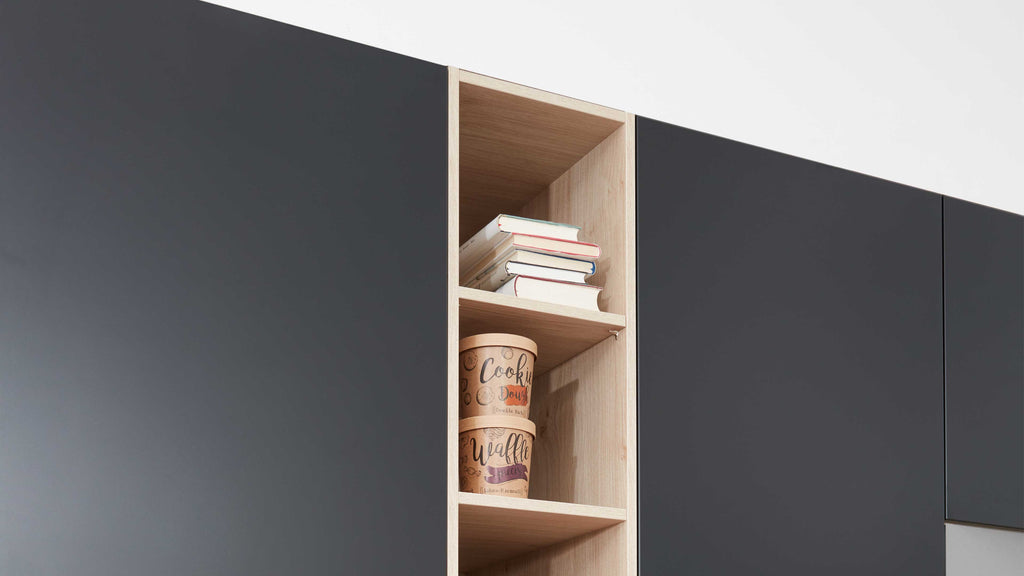 Offenes, helles Regalfach zwischen dunklen Schranktüren mit einem Stapel Bücher oben und zwei runden Dosen darunter.