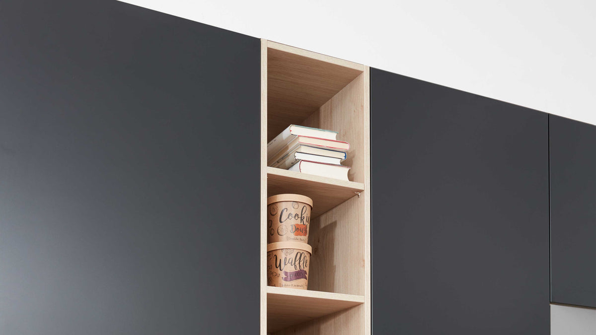 Offenes, helles Regalfach zwischen dunklen Schranktüren mit einem Stapel Bücher oben und zwei runden Dosen darunter.