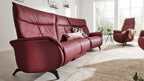 Dreisitziges rotes Ledersofa mit zwei Zierkissen in hellem Wohnzimmer, rechts ein roter Sessel und ein Beistelltisch.