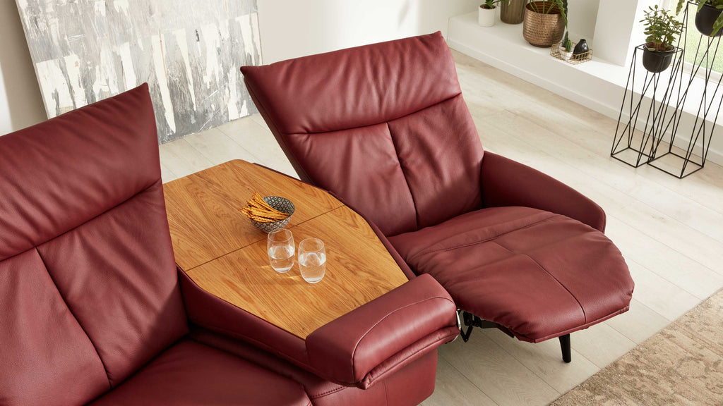 Zweisitziges rotes Ledersofa mit mittlerer Holzablage, darauf zwei Wassergläser und Schale mit dünnen Stäbchen.