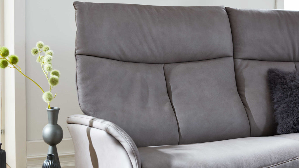 Grau bezogene Sofa-Rücken- und Sitzfläche mit sichtbarer Armlehne, grauem Fellkissen rechts und Vase links.
