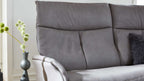 Grau bezogene Sofa-Rücken- und Sitzfläche mit sichtbarer Armlehne, grauem Fellkissen rechts und Vase links.