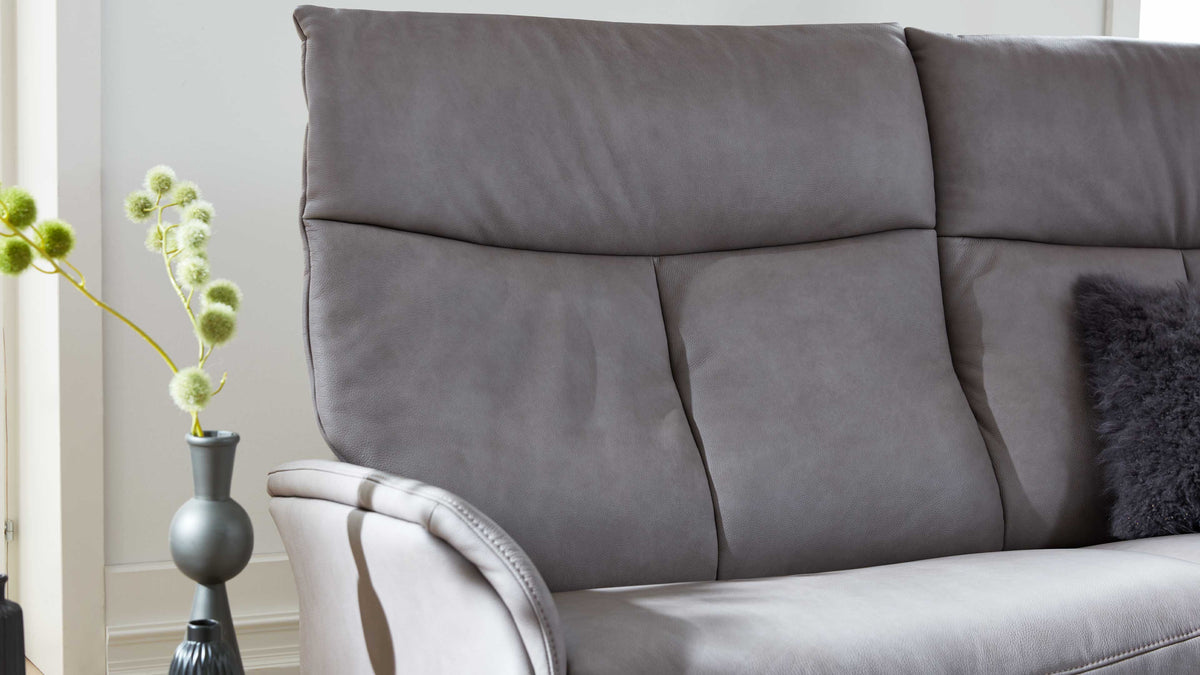 Grau bezogene Sofa-Rücken- und Sitzfläche mit sichtbarer Armlehne, grauem Fellkissen rechts und Vase links.