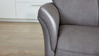 Graues Lederarmteil und Sitzfläche eines Sofas mit sichtbaren Nähten, im Hintergrund Holzboden und weiße Schrankfront.