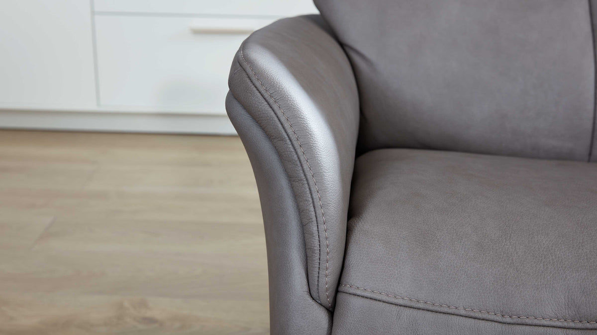 Graues Lederarmteil und Sitzfläche eines Sofas mit sichtbaren Nähten, im Hintergrund Holzboden und weiße Schrankfront.