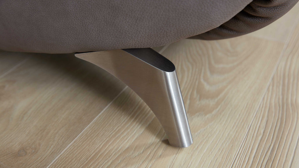Metallfuß eines Sofas mit gebürsteter Oberfläche unter braunem Lederbezug, positioniert auf hellem Holzfußboden.