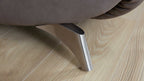 Metallfuß eines Sofas mit gebürsteter Oberfläche unter braunem Lederbezug, positioniert auf hellem Holzfußboden.