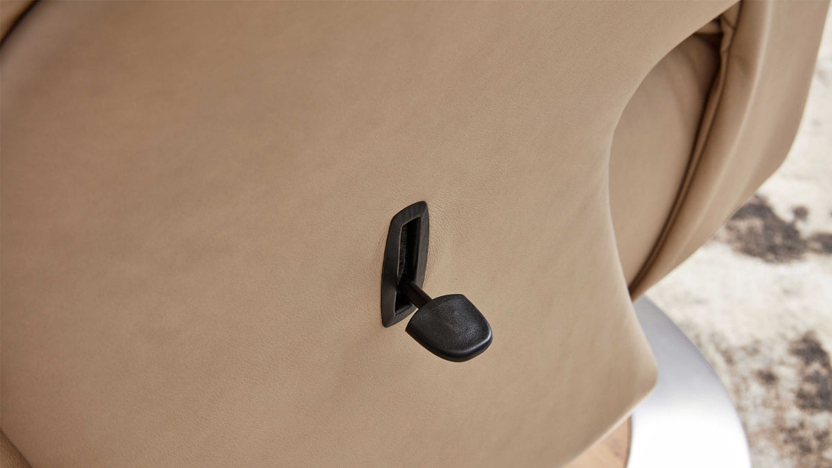 Beiges Leder des Sessels mit schwarzem, schräg stehenden Verstellhebel in rechteckiger Einfassung, seitlich Metallfuß und Teppich.