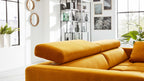 Senfgelbes Sofa mit verstellbarem Kopfteil und einzelnen Kissen, platziert in hellem Raum vor großen Fensterflächen.