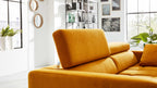 Gelb-orange Stoffsofa mit aufrechter, verstellbarer Kopfstütze, sichtbarem Zierkissen, Regal, Pflanzen und großen Fenstern.