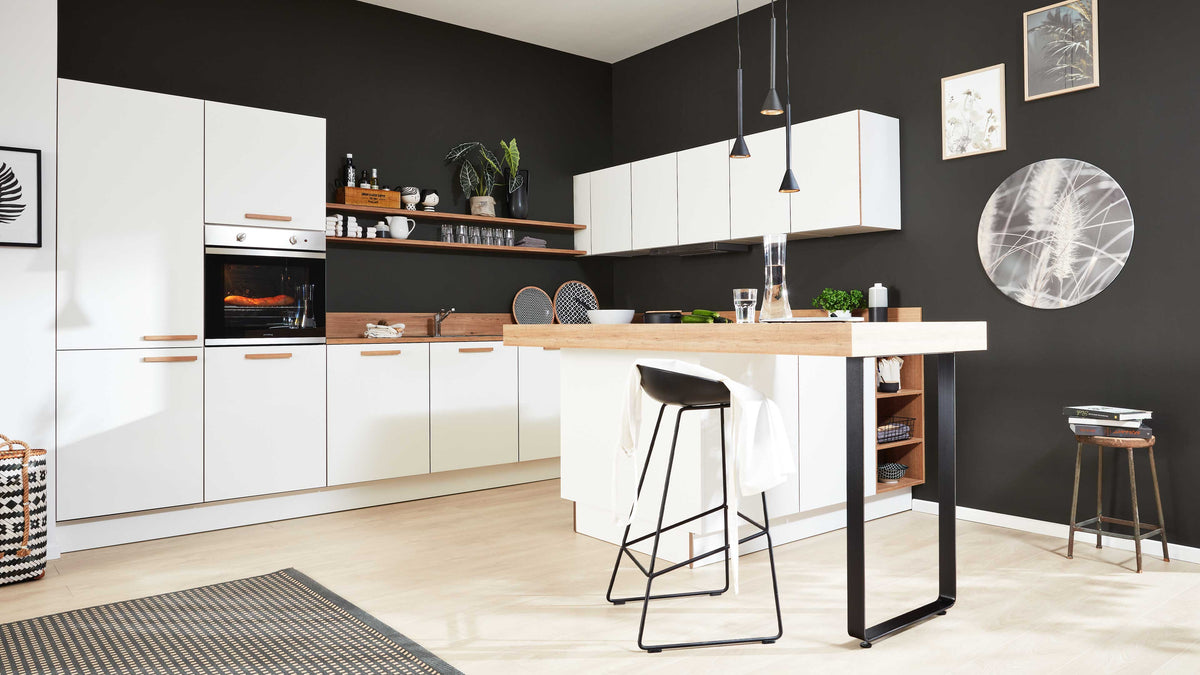 Küche mit weißer Einbauzeile und Holzarbeitsfläche, freistehender Bartisch mit schwarzem Hocker vor schwarzer Wand.