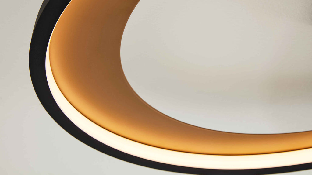 Großformatige Nahaufnahme einer ringförmigen Deckenleuchte mit schwarzem Außenring, goldenem Innenring und weißem Diffusor.