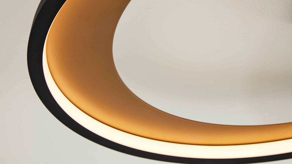 Großformatige Nahaufnahme einer ringförmigen Deckenleuchte mit schwarzem Außenring, goldenem Innenring und weißem Diffusor.
