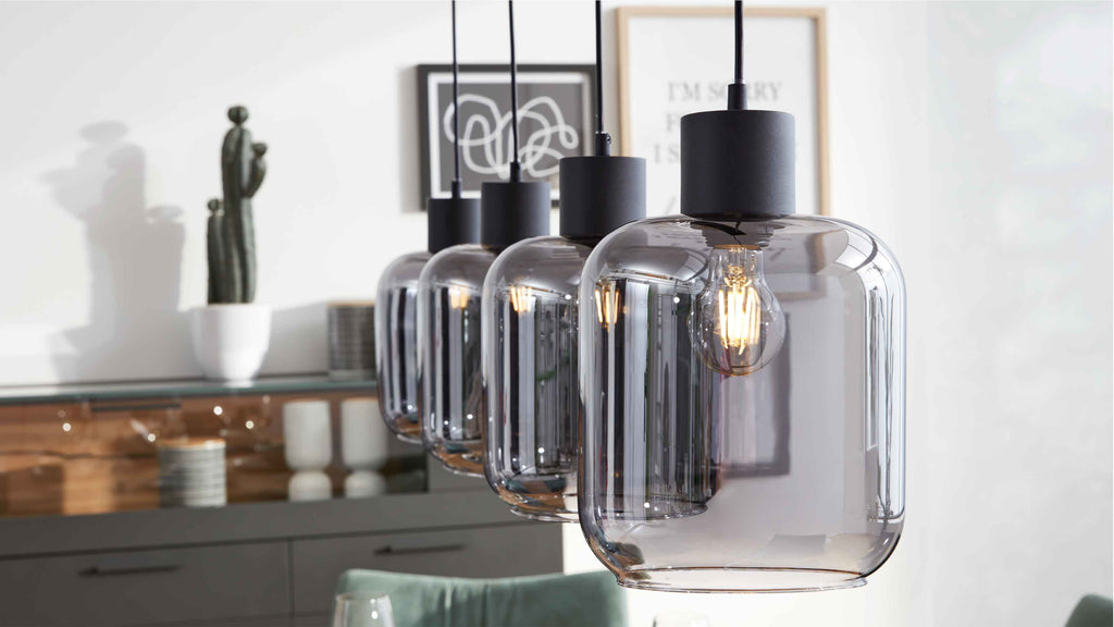 Vier hängende Rauchglas-Pendelleuchten mit schwarzen Fassungen und sichtbaren Filamentbirnen, im Hintergrund Sideboard, Dekor und Kaktus.
