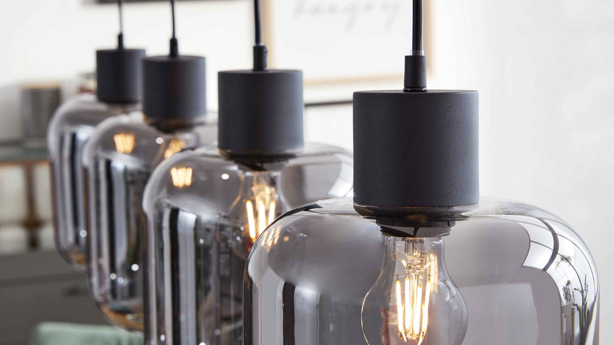 Vorderste Pendelleuchte mit rauchfarbener Glaskuppel, sichtbarer Filament-Glühbirne und mattschwarzem Sockel, dahinter drei Lampen.