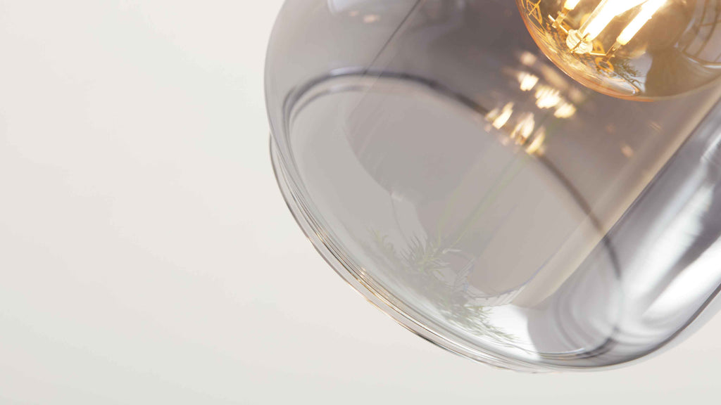 Großaufnahme einer hängenden Glas-Pendelleuchte mit sichtbarer leuchtender Filamentlampe und Reflexionen.