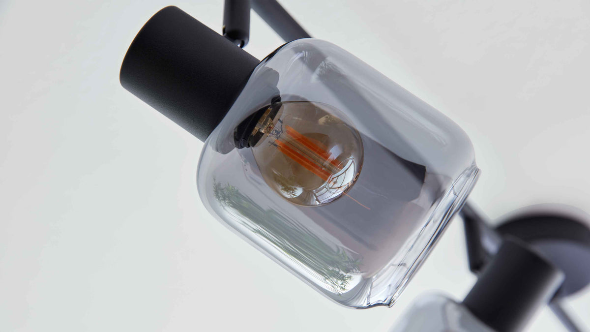 Hängelampe mit rechteckig-gerundeter klarer Glasschale, sichtbare Glühbirne mit orangefarbenen Filamenten und schwarzem Metallhalter.