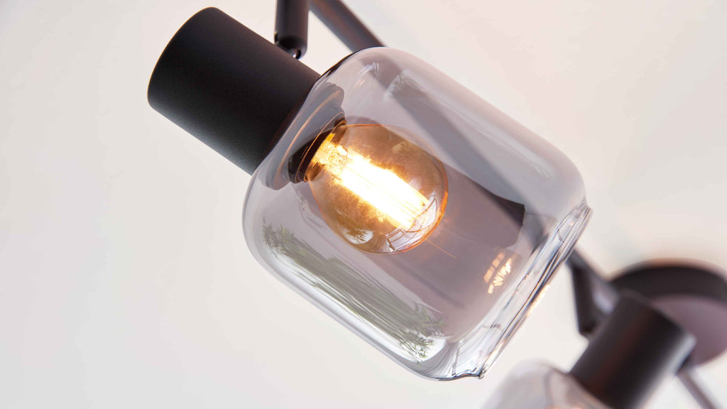 Nahaufnahme einer Hängeleuchte mit klarem gewölbtem Glasschirm, warm leuchtender Glühlampe und schwarzem Metallfassungsarm.