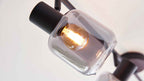 Nahaufnahme einer Hängeleuchte mit klarem gewölbtem Glasschirm, warm leuchtender Glühlampe und schwarzem Metallfassungsarm.