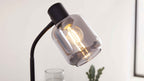 Schwarze Lese- oder Tischlampe mit flexiblem, gewölbtem Arm und rauchfarbenem Glasschirm, darin leuchtende Birne sichtbar.