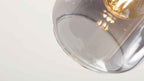 Großaufnahme einer transparenten Glas-Hängeleuchte mit sichtbarer, leuchtender Filamentlampe und Reflexionen im Glas.