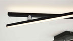 Schwarze, schlanke LED-Leisten kreuzen sich unterhalb der Decke, eine Leiste leuchtet warmweiß, Metallhalter sichtbar.