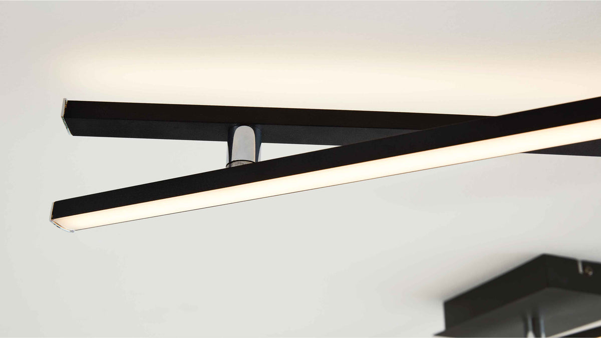 Schwarze, schlanke LED-Leisten kreuzen sich unterhalb der Decke, eine Leiste leuchtet warmweiß, Metallhalter sichtbar.