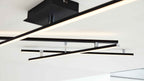 Deckenleuchte mit mehreren sich kreuzenden schwarzen LED-Linienstäben, an silbernen Halterungen an weißer Decke montiert.