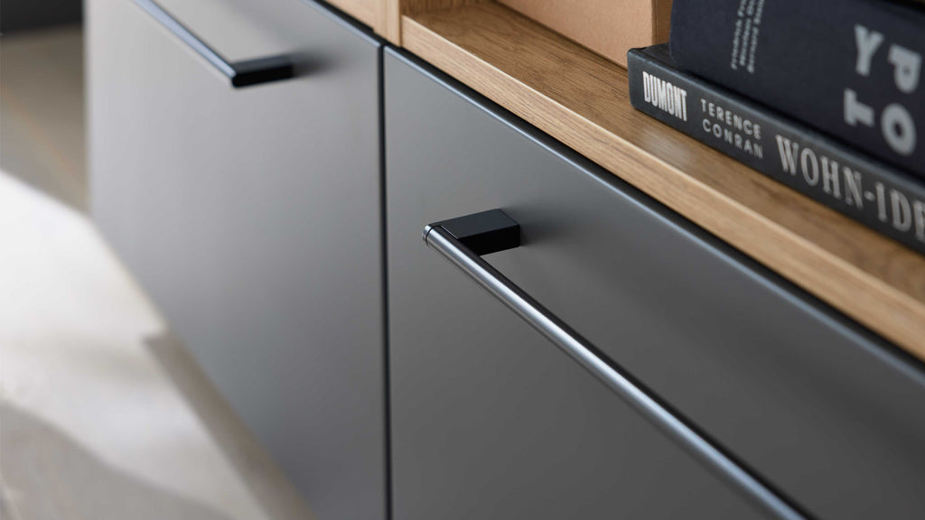 Nahaufnahme einer matten dunkelgrauen Schublade mit langem Metallgriff, Eichenholzoberkante und Büchern.
