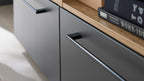 Nahaufnahme einer matten dunkelgrauen Schublade mit langem Metallgriff, Eichenholzoberkante und Büchern.