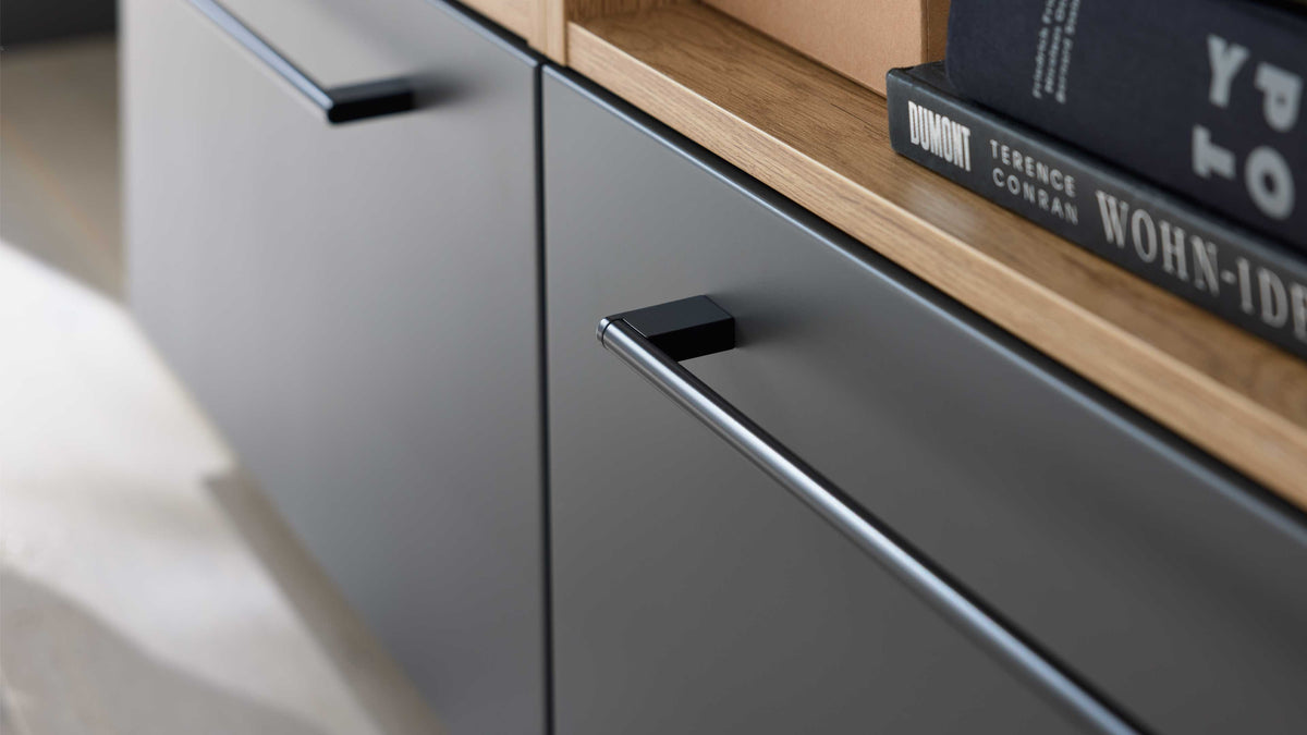 Nahaufnahme einer matten dunkelgrauen Schublade mit langem Metallgriff, Eichenholzoberkante und Büchern.