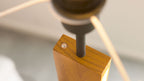 Obere Kante eines rechteckigen Holzblocks mit eingelassenem Metallstift, runden Schraubenkopf und angesetztem Lampenrohr.