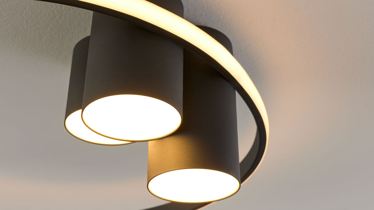Deckenleuchte mit schwarzen, zylindrischen Schirmen an einem gebogenen LED-Ring, warmes Licht nach unten.