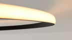 Rundliche, leuchtende Deckenlampe mit warmweißem Diffusor und schwarzem Innenteil, Decke im Hintergrund.