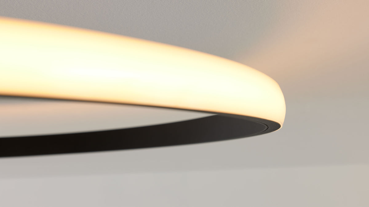 Rundliche, leuchtende Deckenlampe mit warmweißem Diffusor und schwarzem Innenteil, Decke im Hintergrund.