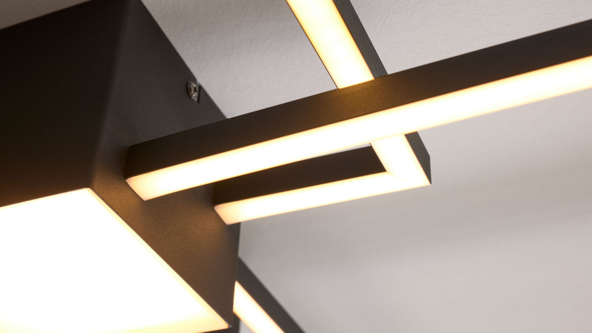 Schwarze, eckige Deckenleuchte mit mehreren horizontalen Leuchtstäben und opalen Diffusoren an einer weißen Decke.