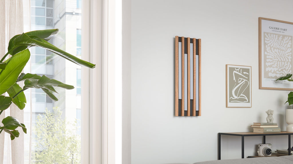 Vertikal montiertes Holzpaneel mit fünf senkrechten Lamellen und hellen Einsätzen an weißer Wand, rechts Bilder und Konsole.