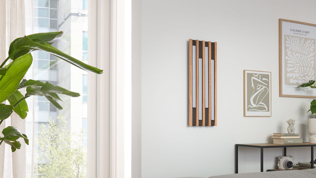 Vertikal montiertes Holzpaneel mit fünf senkrechten Lamellen und hellen Einsätzen an weißer Wand, rechts Bilder und Konsole.