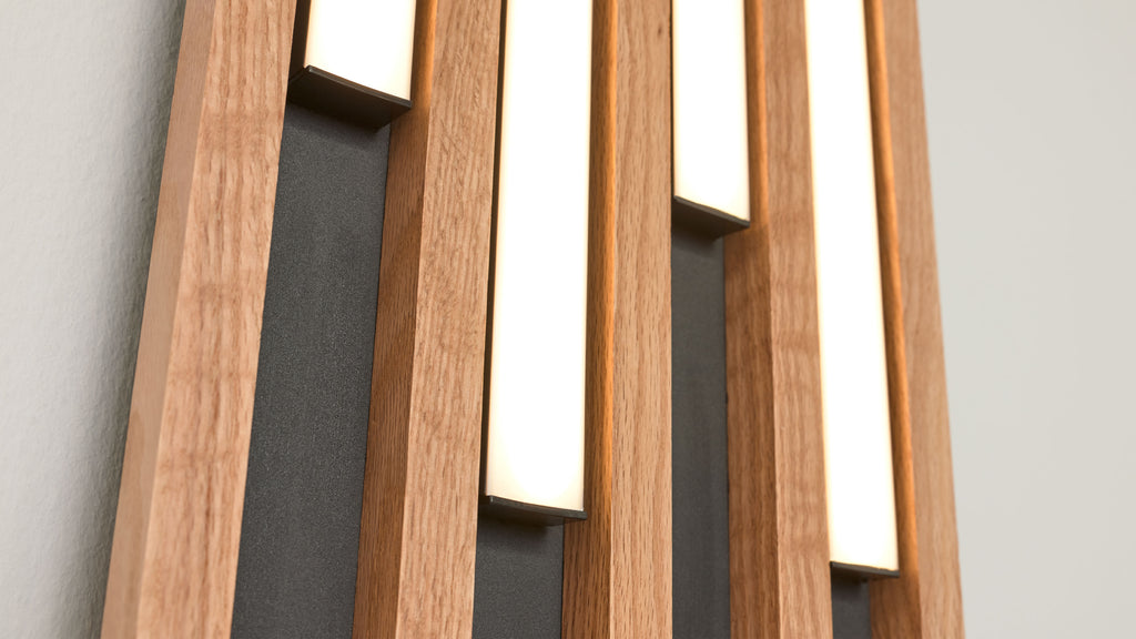 Vertikale Holzlamellen mit drei eingelassenen schmalen, beleuchteten Leuchtpanelen vor dunklen Rückplatten und heller Wand.