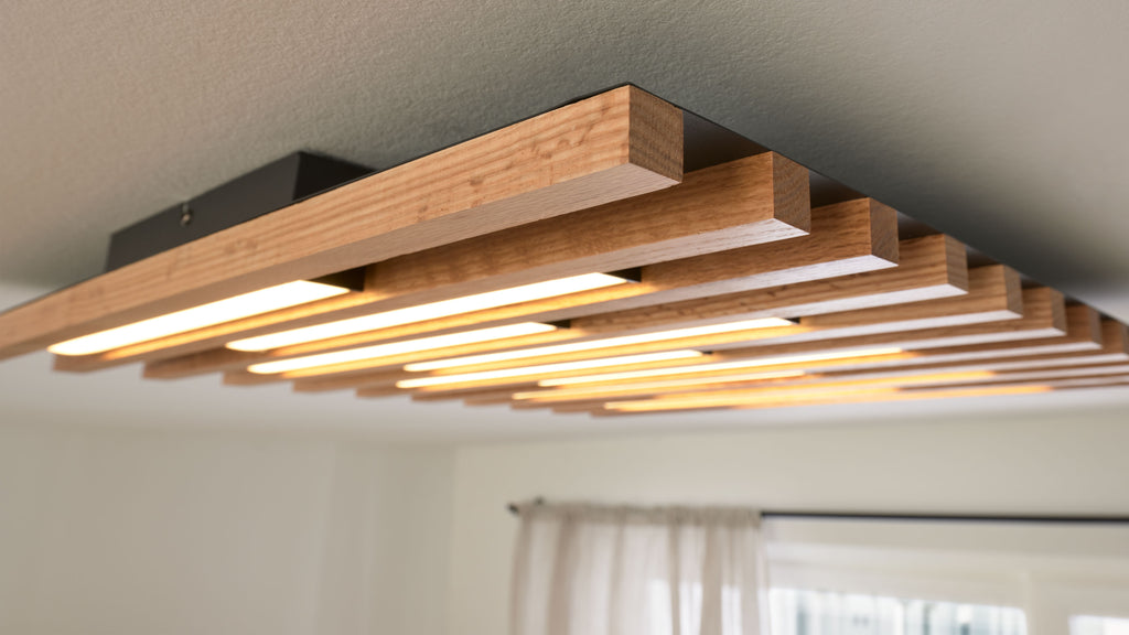 Rechteckige Deckenleuchte mit horizontalen Holzlamellen und integrierten warmen LED-Streifen, schwarzer Montagekasten sichtbar.