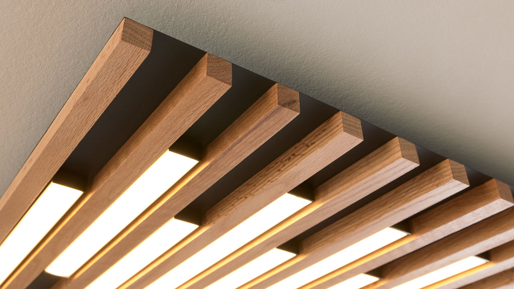 Deckenleuchte aus parallelen eichenfarbigen Holzlamellen, zwischen denen schwarze Träger und längliche warme LED-Leuchtfelder sitzen.