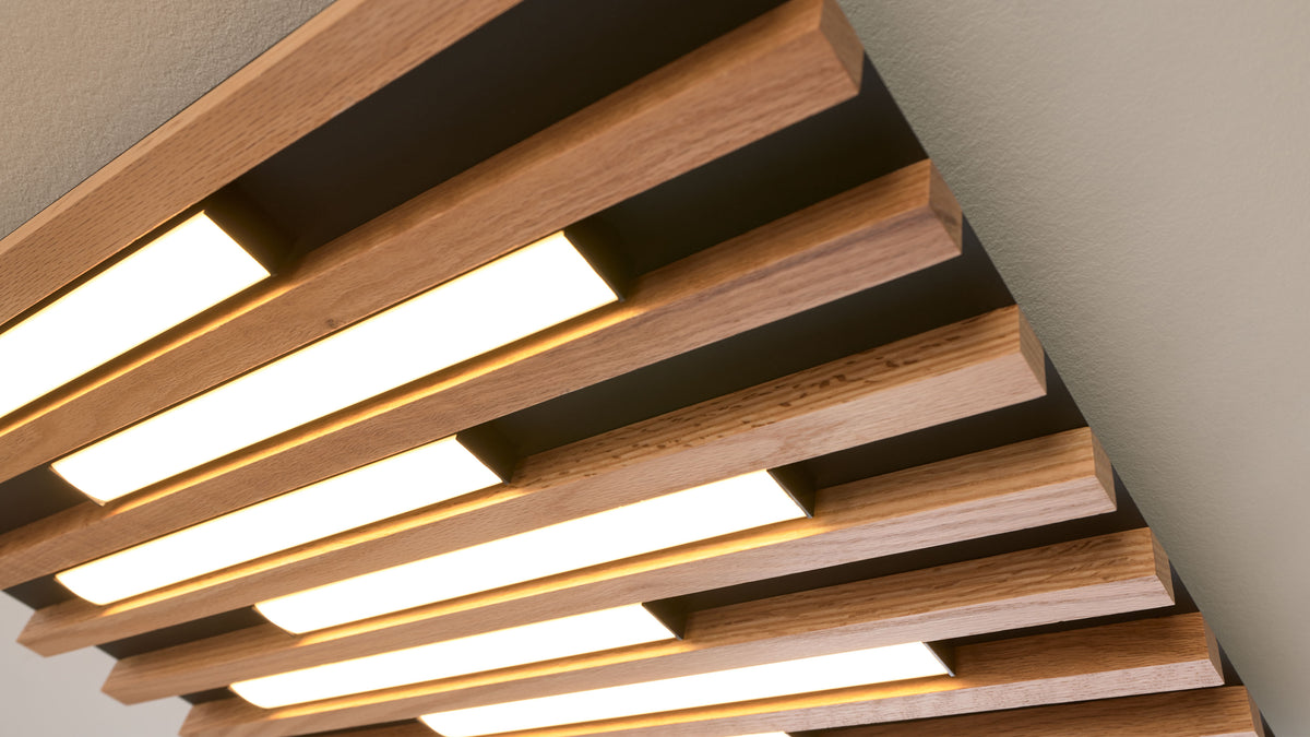Deckeninstallation aus parallelen Holzlamellen mit eingelassenen rechteckigen, warm leuchtenden LED-Paneelen in schwarzem Rahmen.