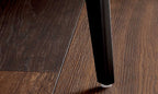 Schwarzes Stuhlbein auf dunkelbraunem Holzboden neben einem ZEHDENICK IL Serie 4306 Jubiläums-Edition-Ecksofa mit sichtbarer Maserung.
