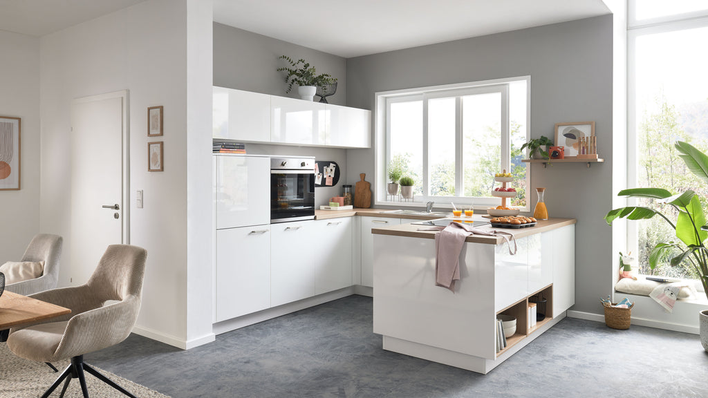 Helle, moderne Küche mit weißen Hochglanzfronten, Holzarbeitsplatte, Fensterbank mit Pflanzen und einem Tisch mit Stühlen.