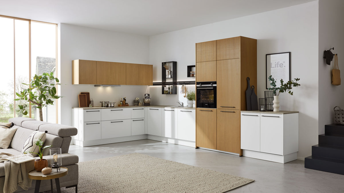 Eine moderne Küche in Weiß und Holz mit Ober- und Unterschränken, einem Kochfeld, Backofen und einer offenen Wohnzone mit Sofa und Teppich.