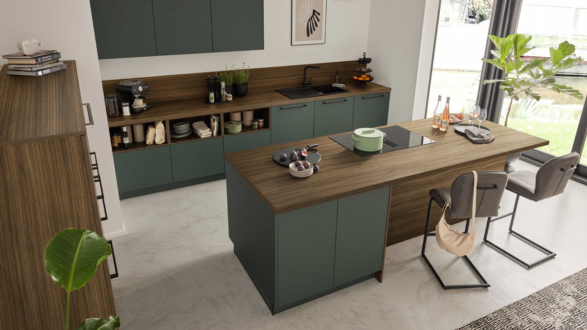 Küche mit mittiger Holz-Arbeitsinsel mit grün lackierten Fronten, Induktionsfeld, Tellern, zwei Barhockern.